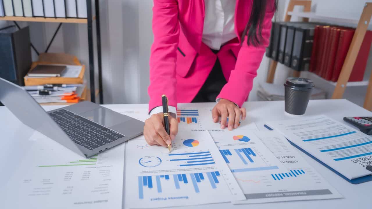 Mulher no escritório com vários papéis na mesa com gráficos e números para analisar as contas a pagar da empresa.