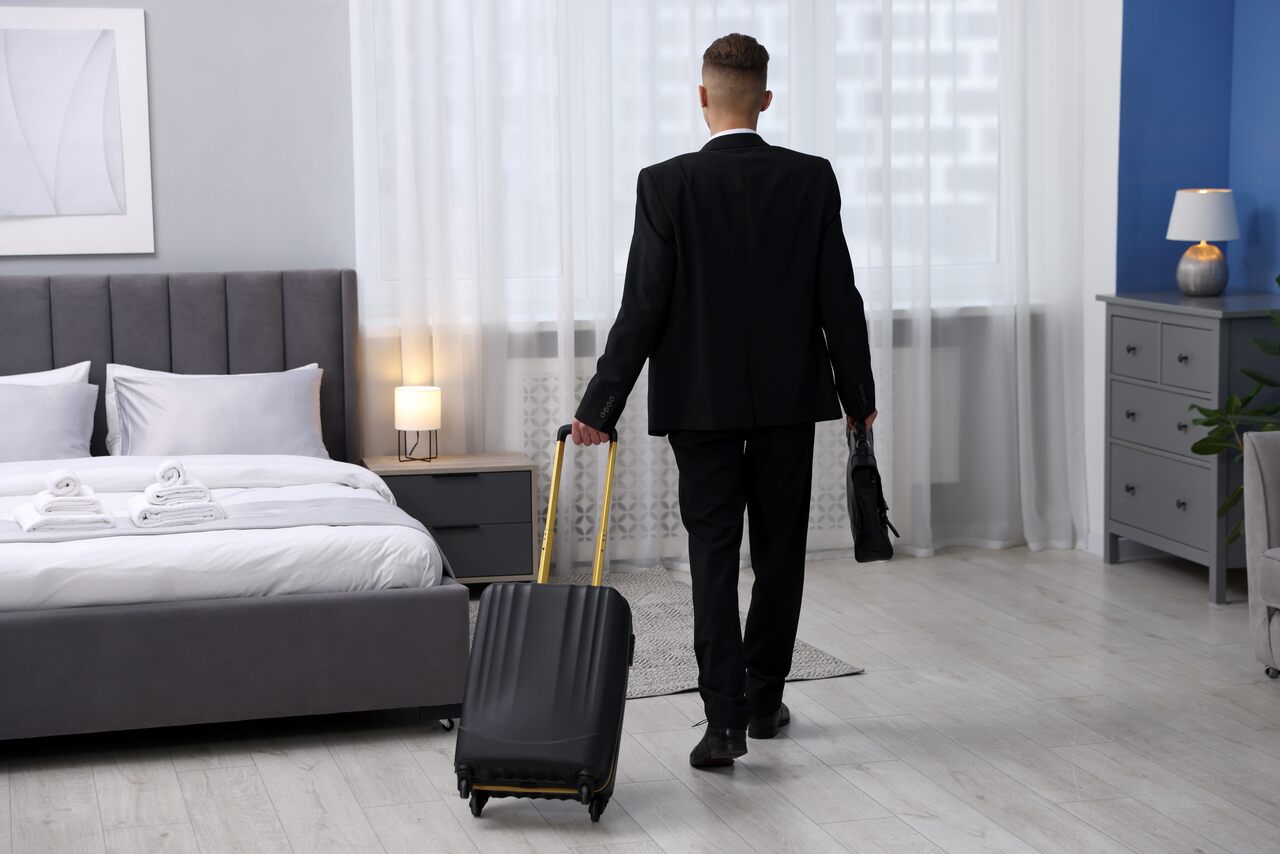 Profissional dentro de um quarto de hotel com sua mala de viagem a fim de mostrar os diversos tipos de hospedagem em viagens corporativas,
