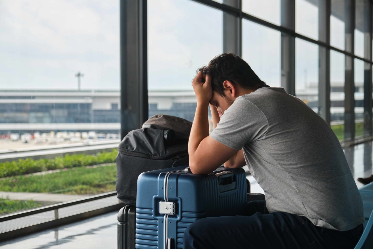 Colaborador de uma empresa em um aeroporto com as mãos na cabeça preocupado com o seu voo cancelado.