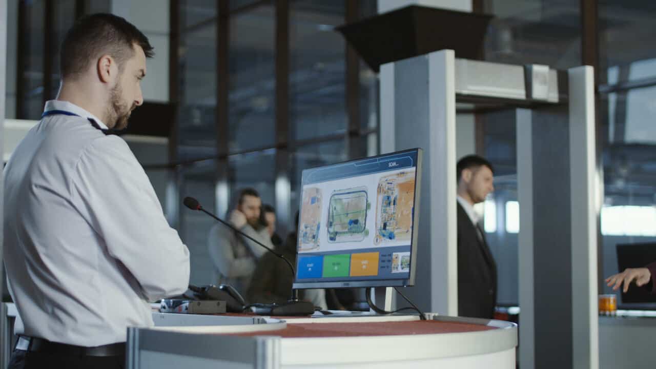 Agente de segurança do aeroporto analisando o conteúdo de uma mala que está na esteira de raio-x.