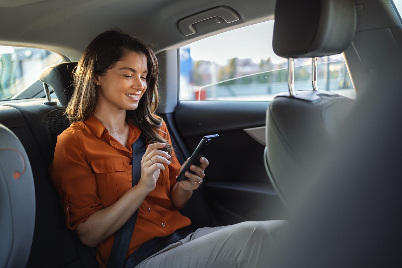 Mulher dentro de um carro usando o celular durante translado em viagens corporativas.