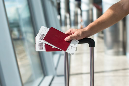 Pessoa segurando duas passagens aéreas dentro de um aeroporto para falarmos sobre o reembolso de passagem aérea.