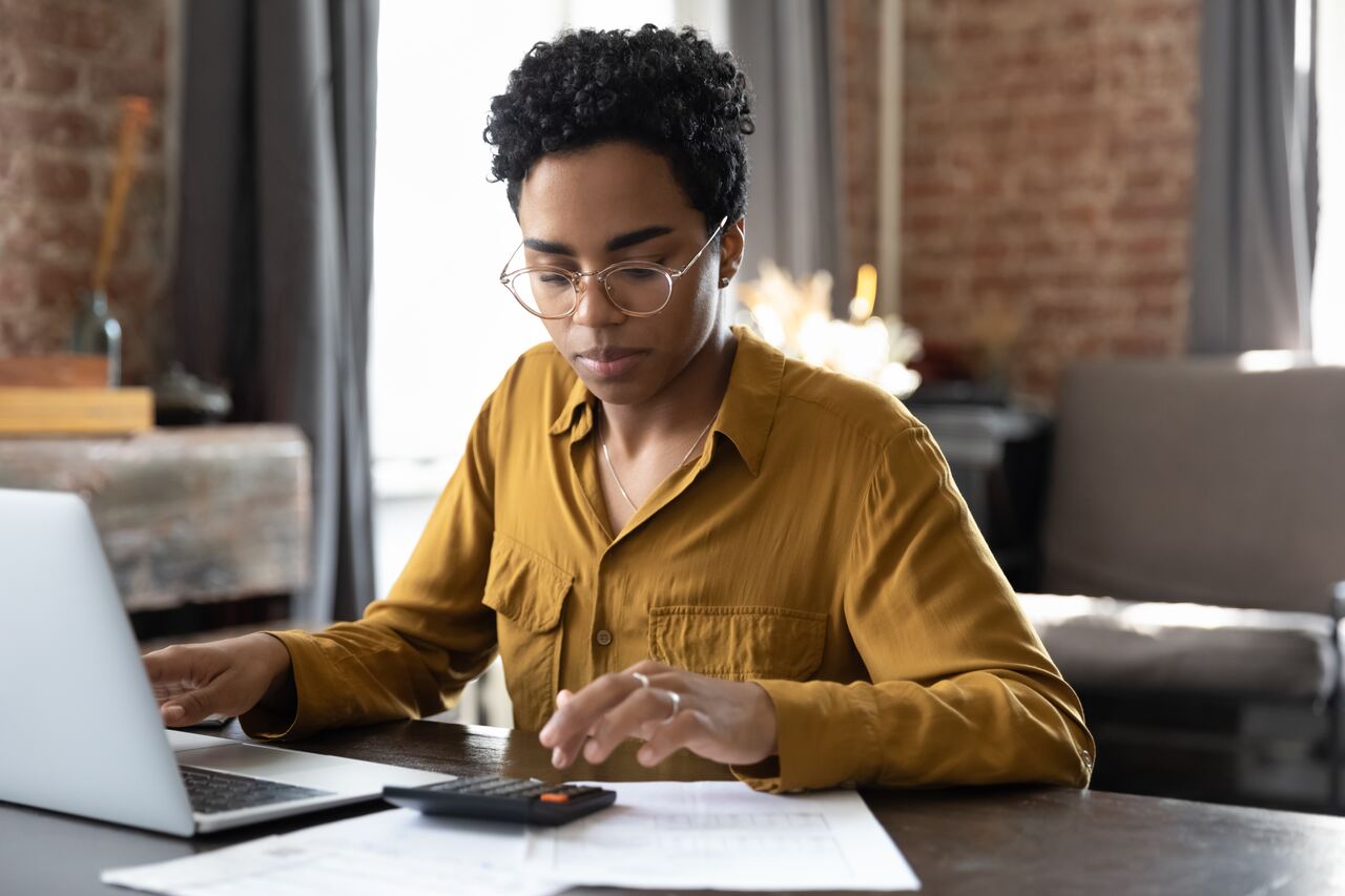 mulher com blusa bege trabalhando no escritório com um notebook e uma calculadora avaliando o risco de crédito.