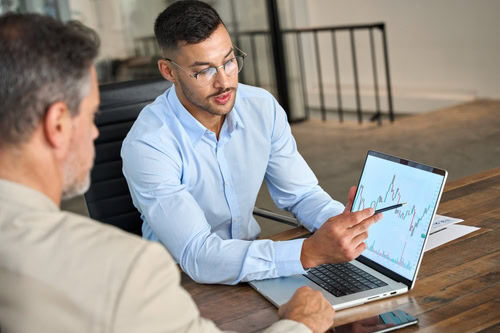 Dois homens analisando uma tela com um gráfico, a fim de avaliar a liquidez geral da empresa.
