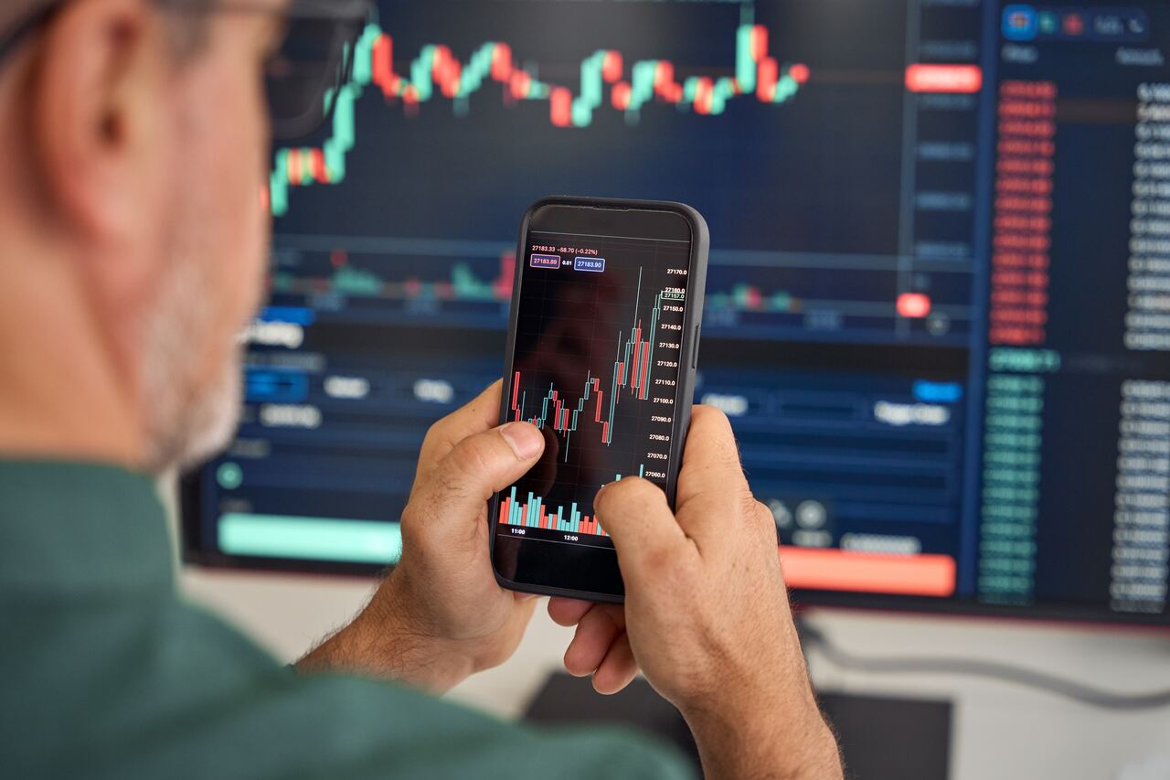 profissional analisando gráficos em seu celular e em uma tela ao fundo, a fim de entender o que é forex.