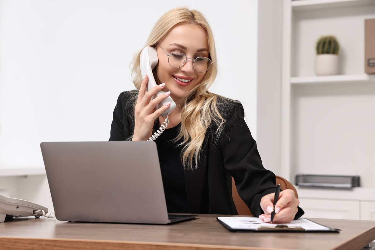 Mulher trabalhando em seu escritório enquanto fala no telefone para destacarmos o papel das secretárias nas viagens corporativas.